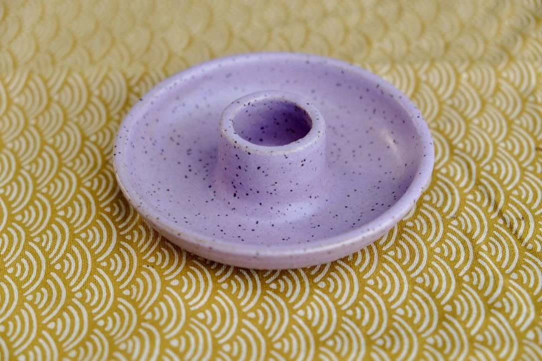 Handmade wheel-thrown lilac ceramic candle holder sits on a yellow table cloth.