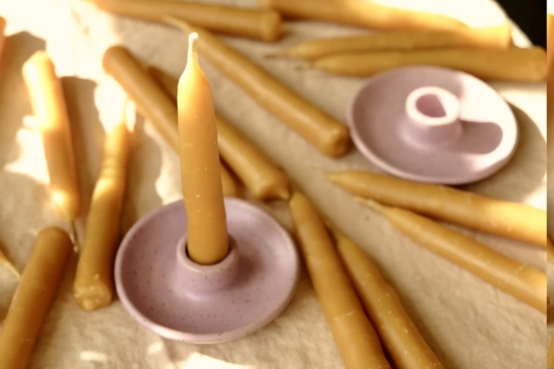 Hand-dipped beeswax taper candles and lilac colored ceramic candle holders lay on a tan table cloth.