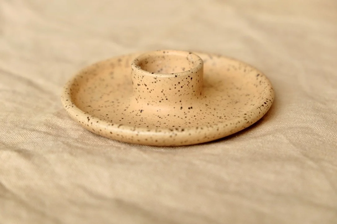 Handmade wheel-thrown papaya colored ceramic candle holder sits on a tan table cloth.