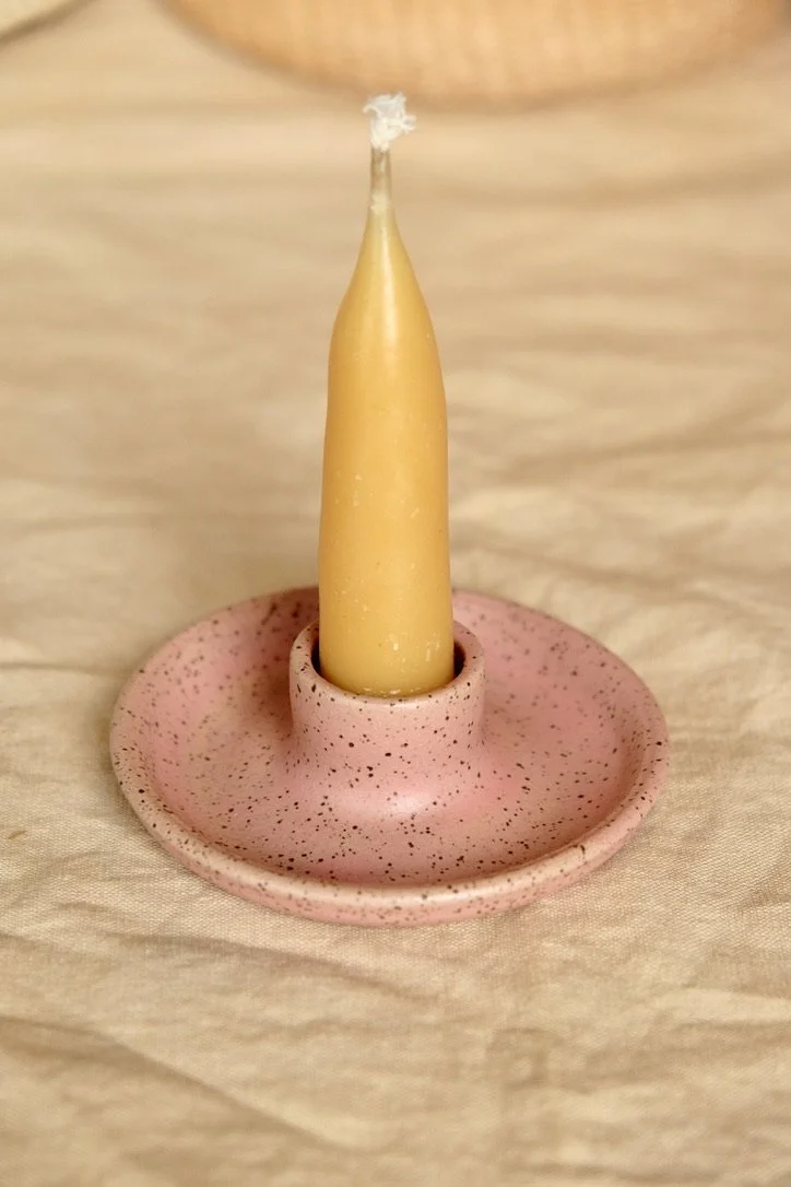 Hand-thrown ceramic watermelon colored candle holder sits on a tan table cloth, with a beeswax candle in the holder.