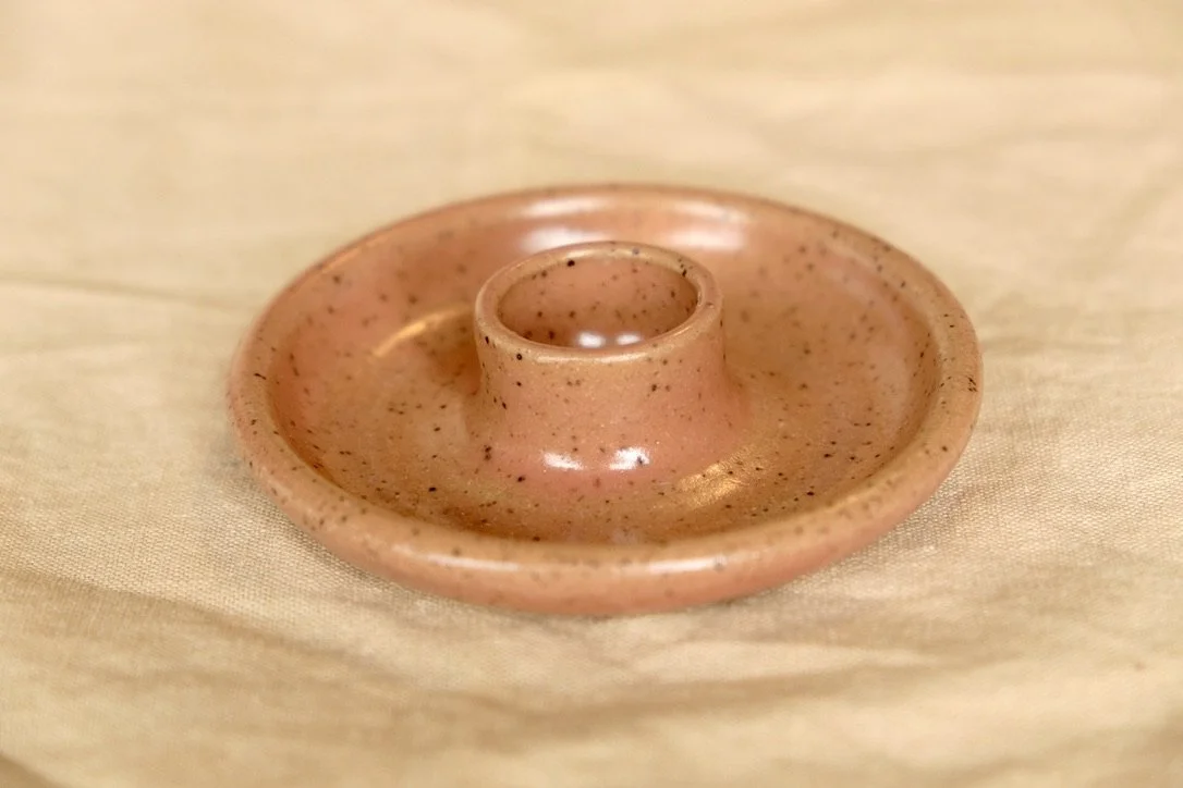 Hand-thrown circular ceramic candle holder in rose hip glaze, resting on linen cloth.