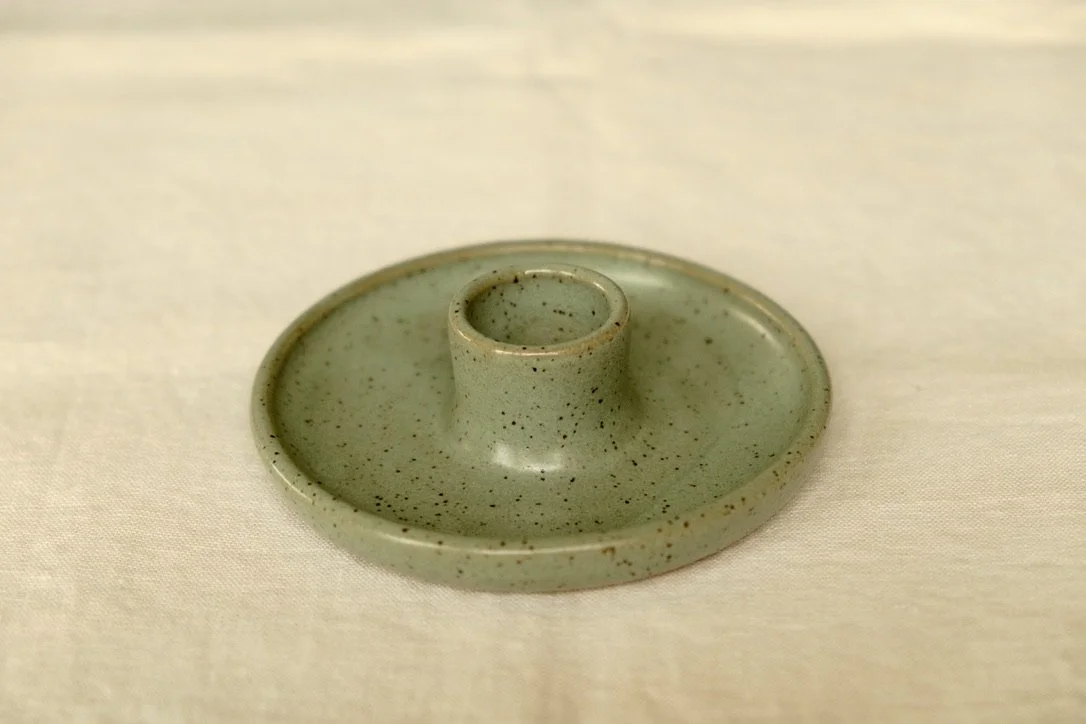 Hand-thrown ceramic avocado green candle holder sits on a tan table cloth.