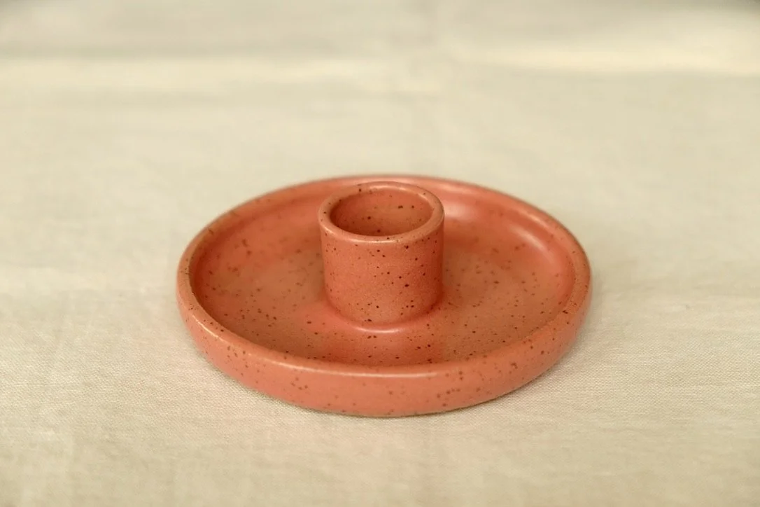 Hand-thrown ceramic coral colored candle holder sits on a tan table cloth.
