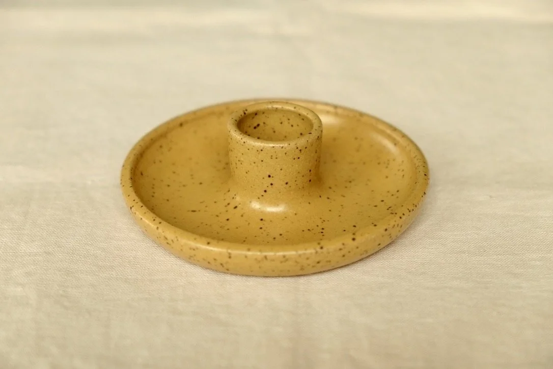 Hand-thrown ceramic mustard yellow candle holder sits on a tan table cloth.