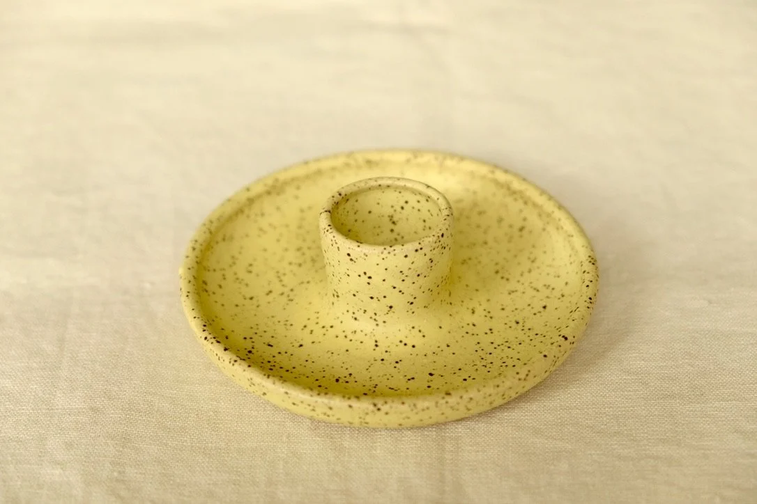 Hand-thrown ceramic lemon yellow candle holder sits on a tan table cloth.