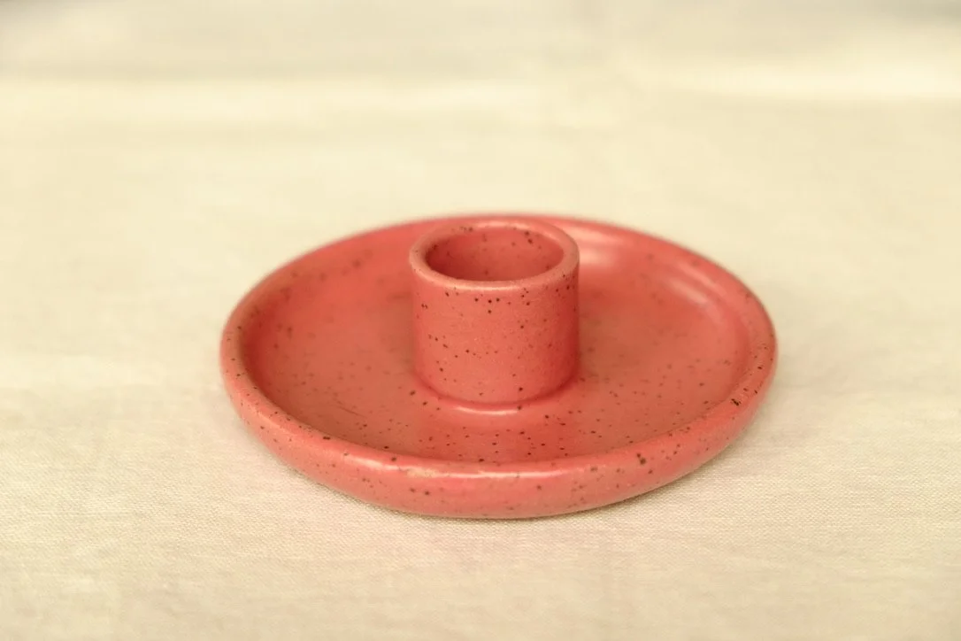 Hand-thrown ceramic raspberry colored candle holder sits on a tan table cloth.