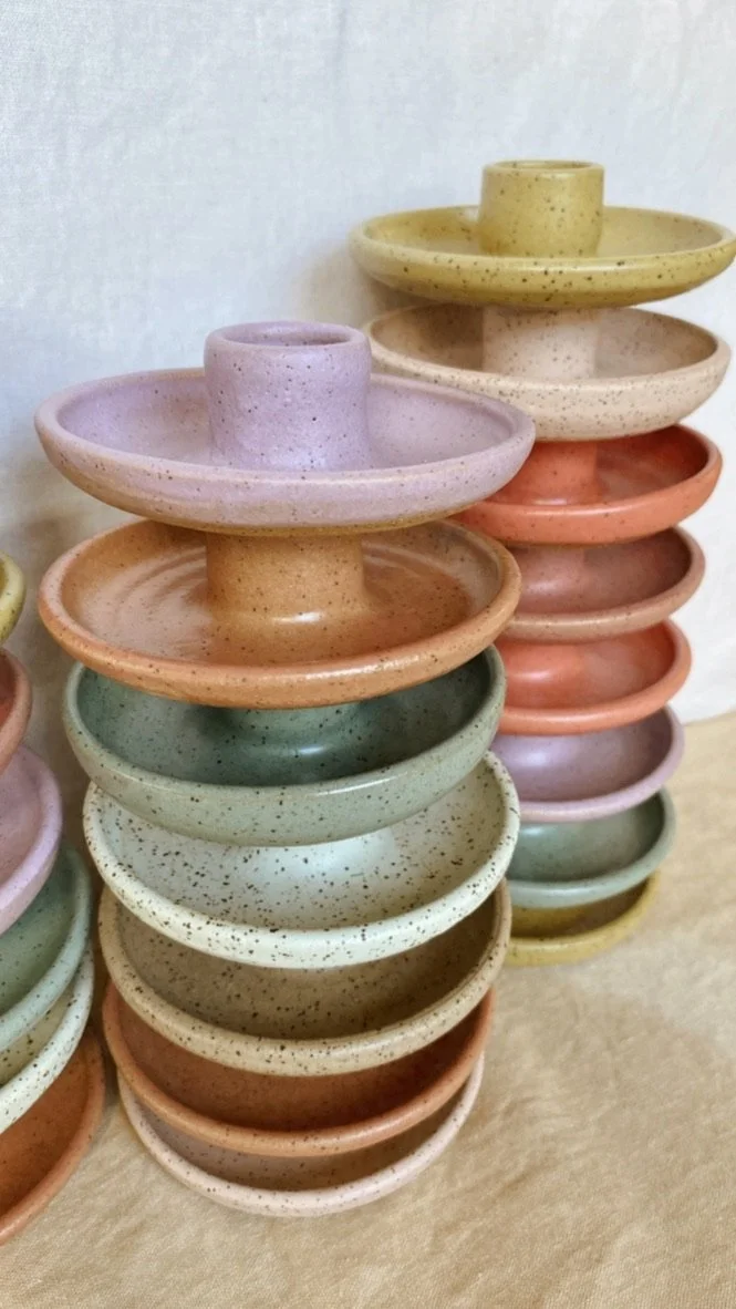 Handmade wheel-thrown ceramic candle makers are stacked into two columns, each candle holder a unique color.