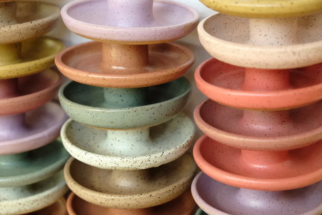 Hand-thrown circular ceramic candle holders stacked in two columns, each glazed in a unique color.