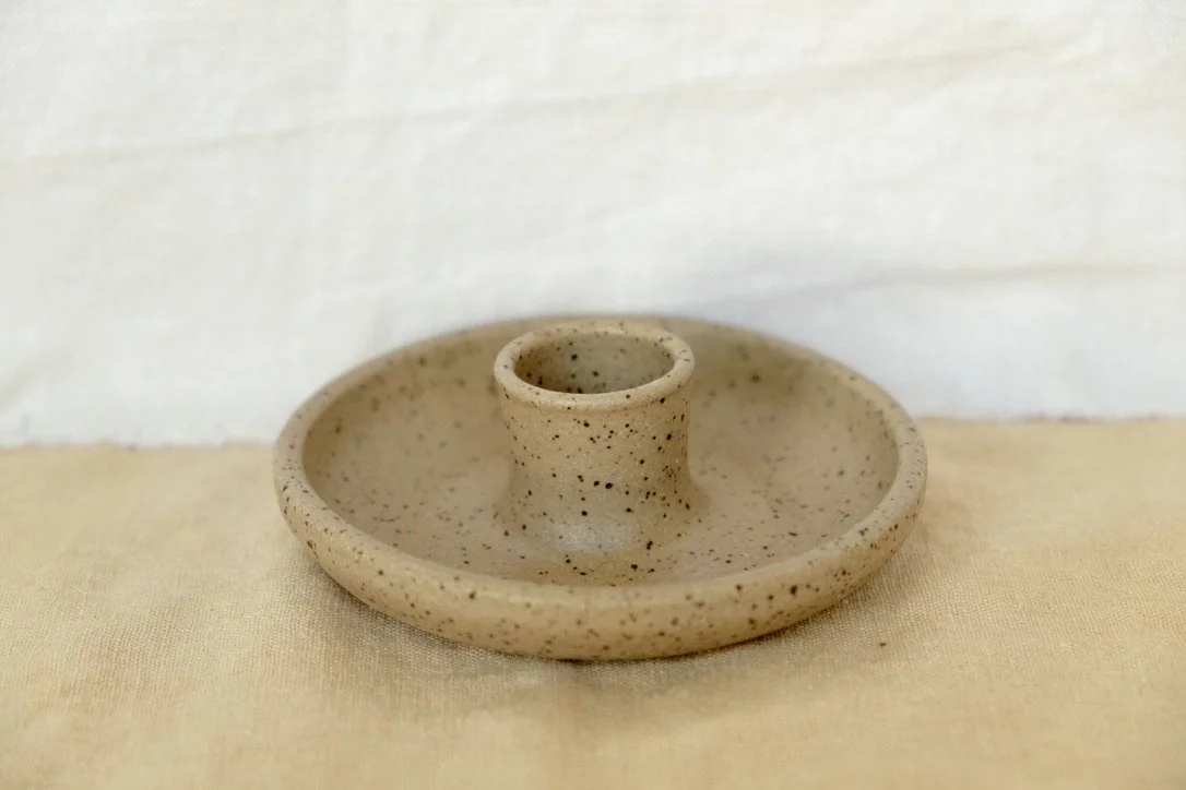 Hand-thrown ceramic oatmeal colored candle holder sits on a tan table cloth.