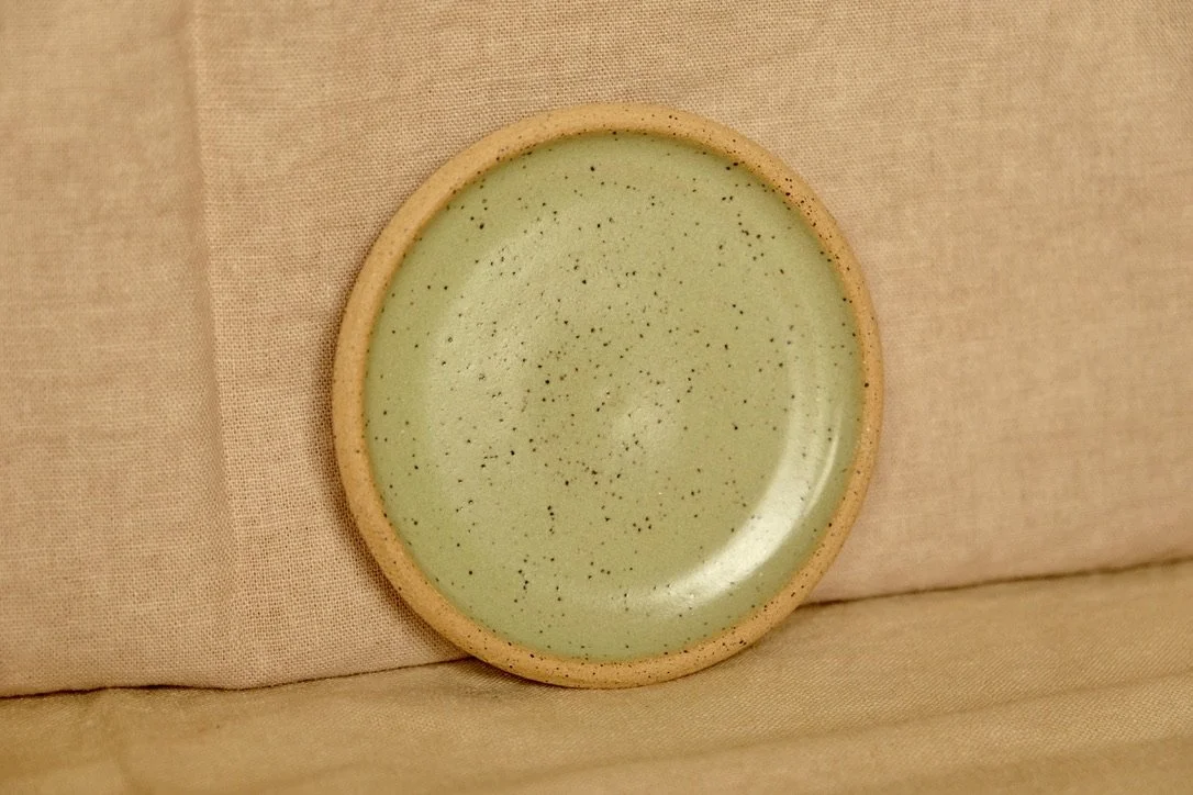 Hand-thrown ceramic ring dish glazed with melon green glaze, resting against warm tablecloth background.