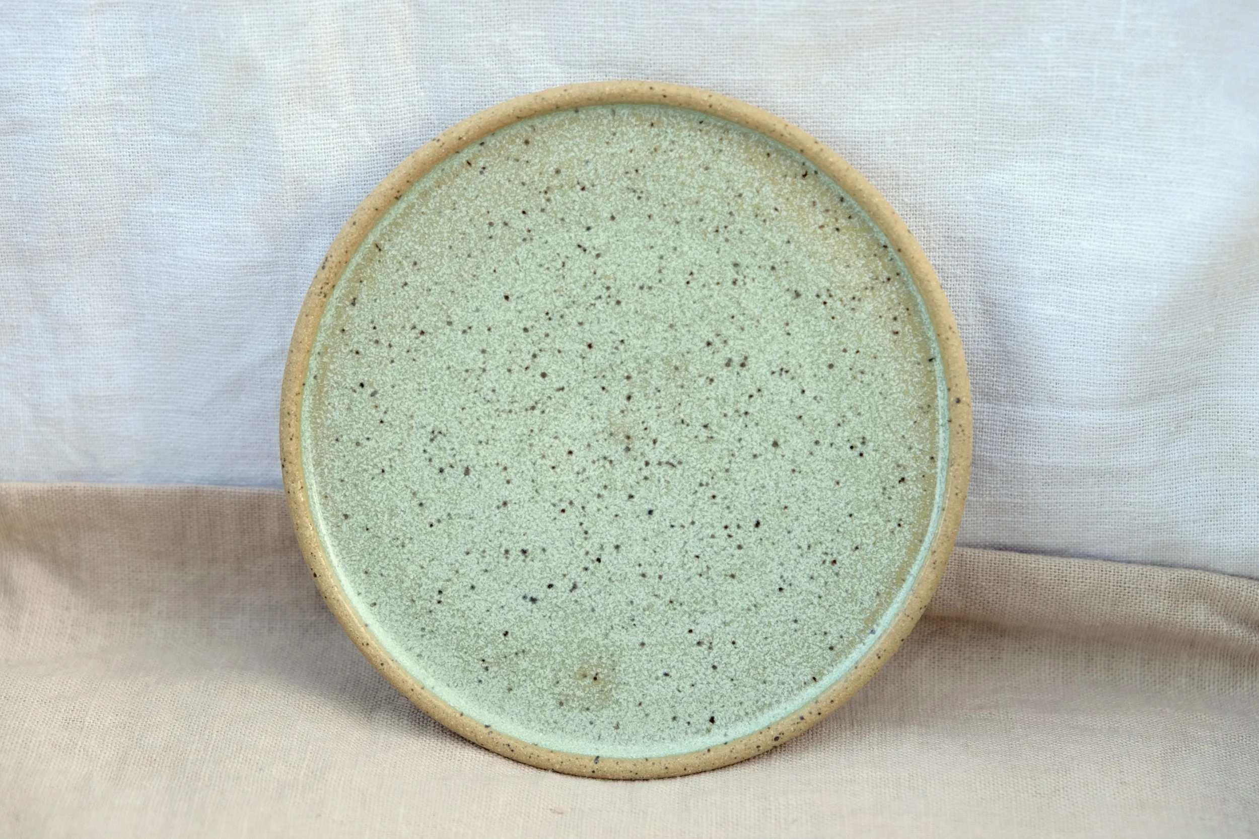 Hand-thrown ceramic ring dish glazed with oceanic blue/green glaze, resting against warm tablecloth background.