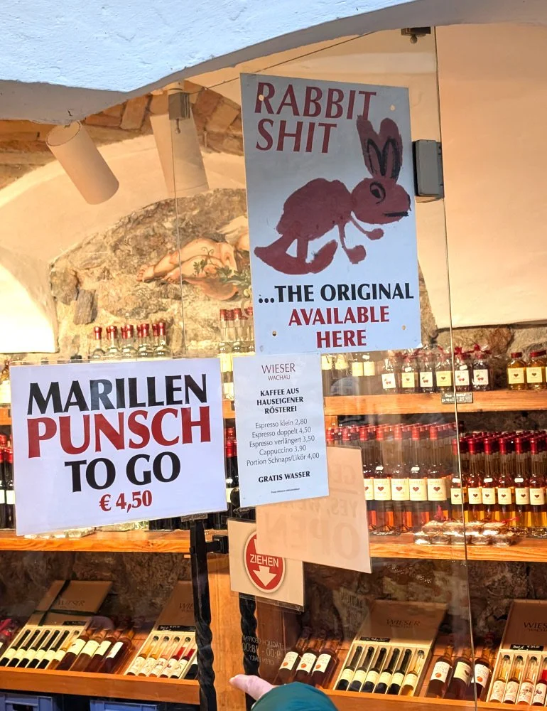 the Wieser Wachau shop window in Dürnstein with humorous signage for items like Rabbit Shit and bottles of apricot products in the background