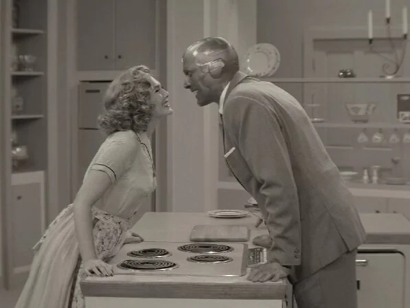Wanda and Vision in black and white, leaning toward each other over a kitchen stove. ©Marvel Studios 2021. All Rights Reserved.