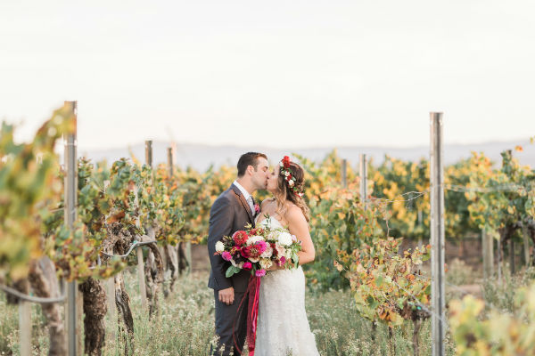 Bride &amp; groom kissing between vineyard rows