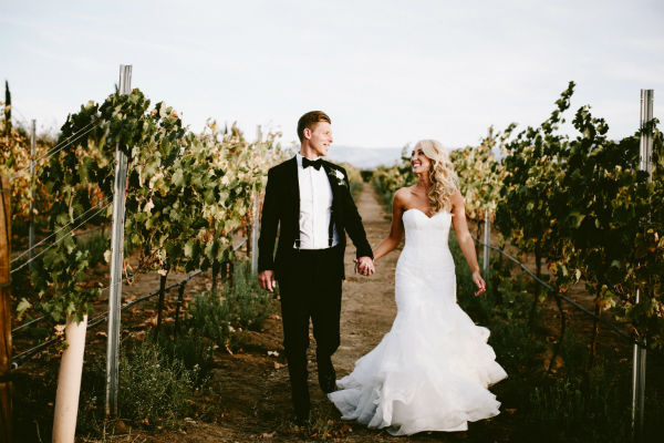 Bride and groom between vinyard rows holding hands