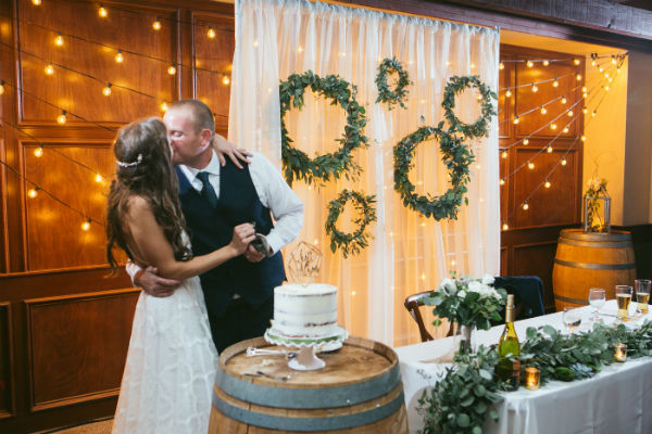 Bride &amp; groom kissing behind the barrel holding the uncut cake