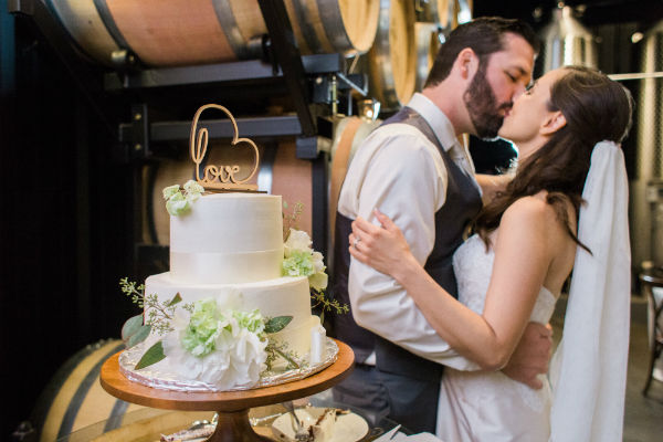 Bride &amp; groom kissing beside 2-tier wedding cake
