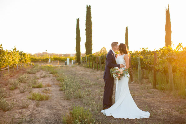 Bride &amp; groom kissing with vineyard in background