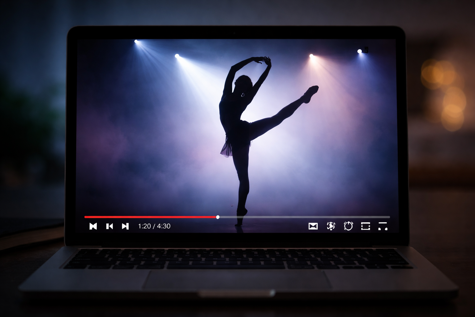 Silhouette of a female ballet dancer performing an arabesque on a stage with dramatic lighting, watched on a laptop screen.
