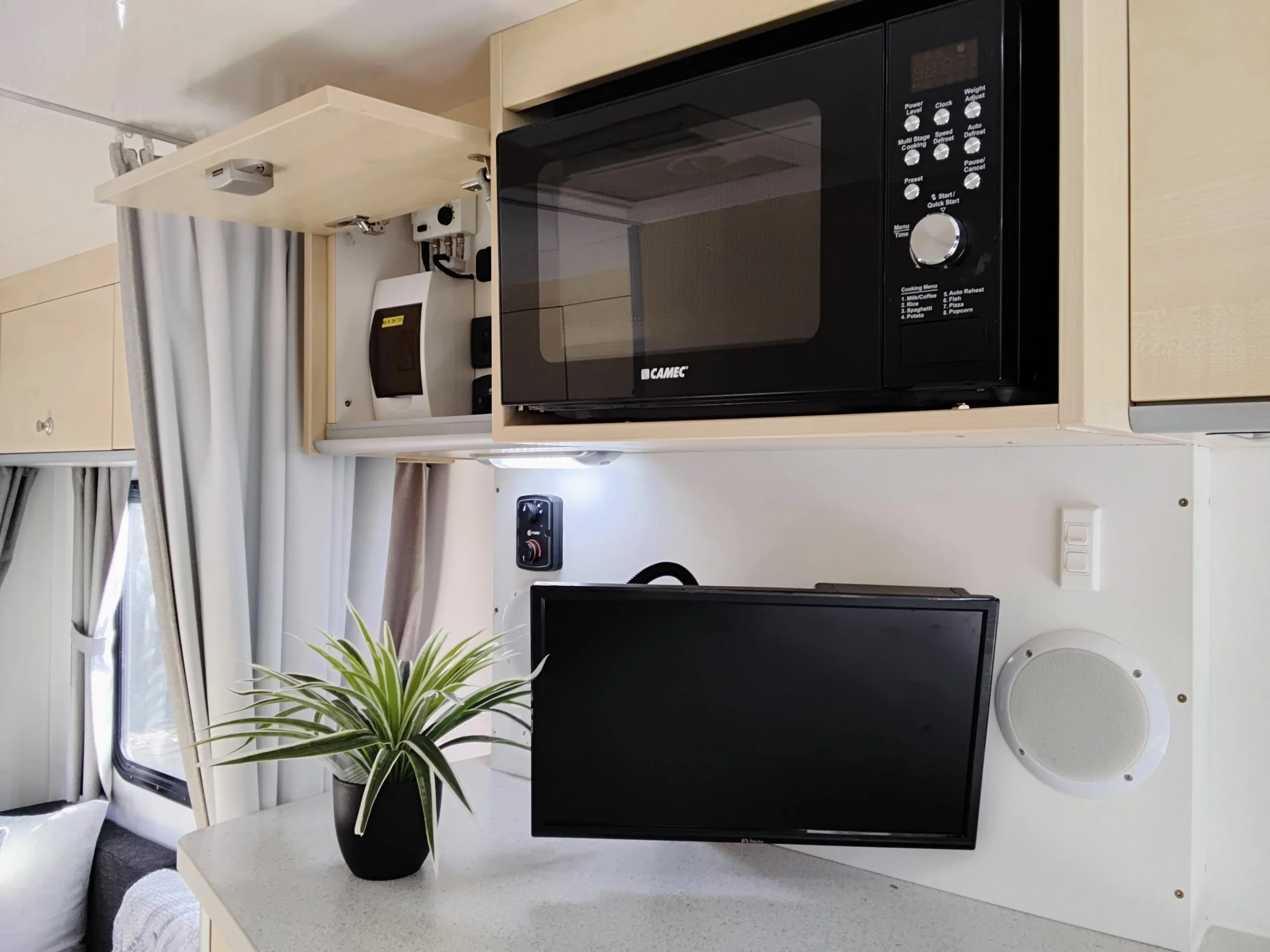 Interior of the Mojo Campers Leo motorhome showing the overhead microwave, swivel mounted TV and speaker above the kitchen bench