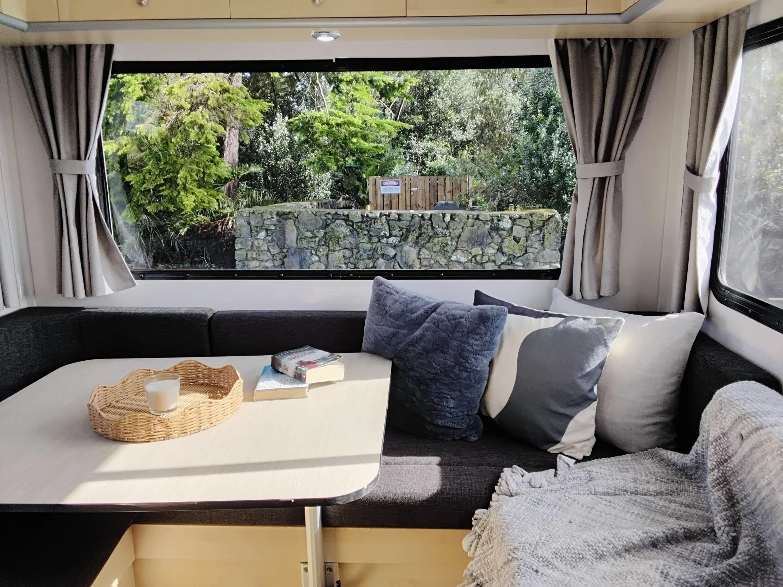 Rear lounge of the Mojo Campers Leo motorhome with wraparound seating, cushions and a large window looking out to native bush
