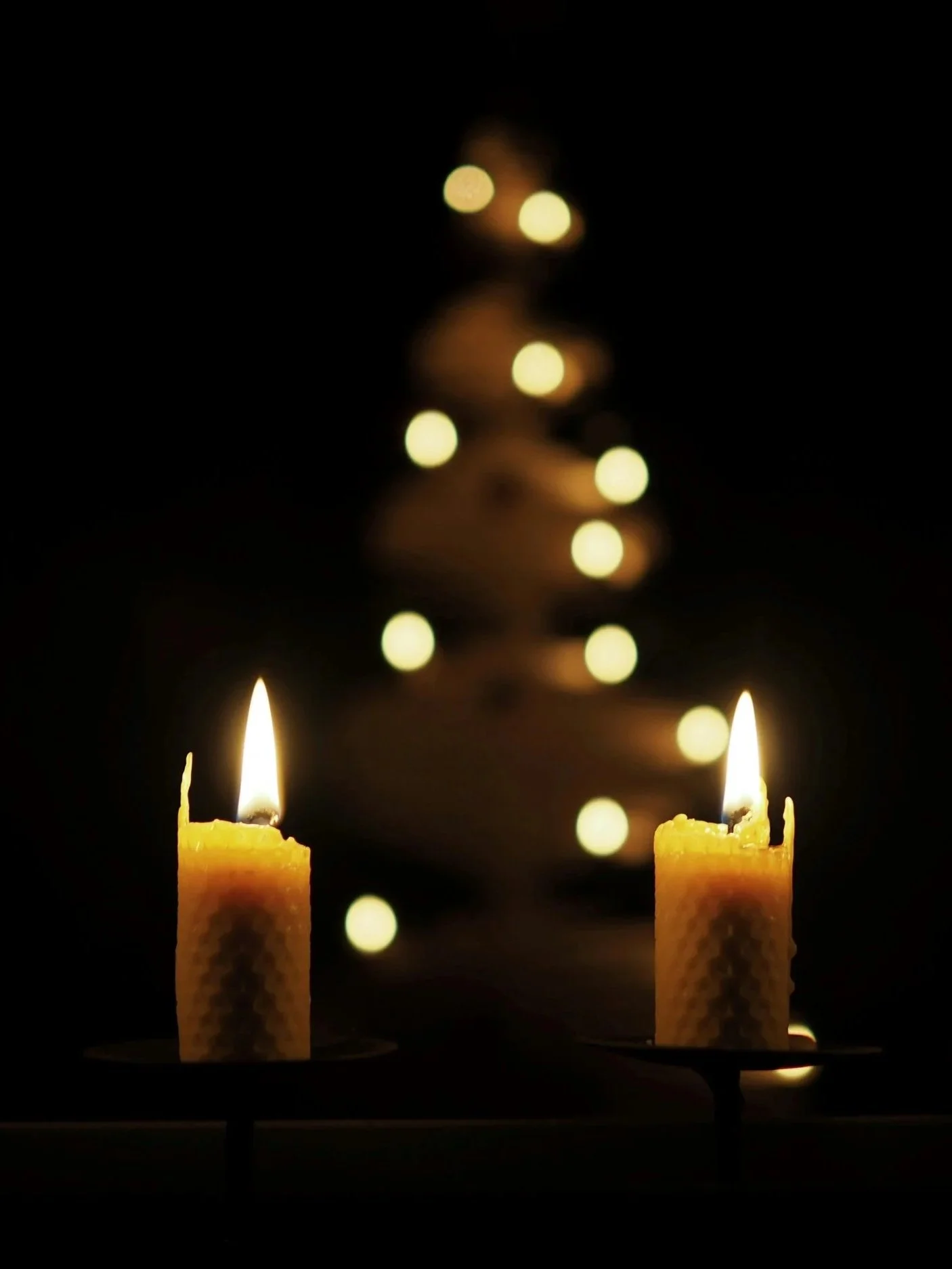 Two lit beeswax candles with a blurred Christmas tree in the background