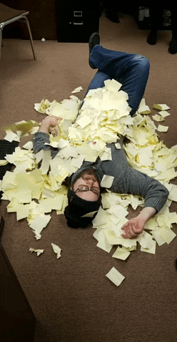 gif of a worker buried under an avalanche of yellow stickie notes.