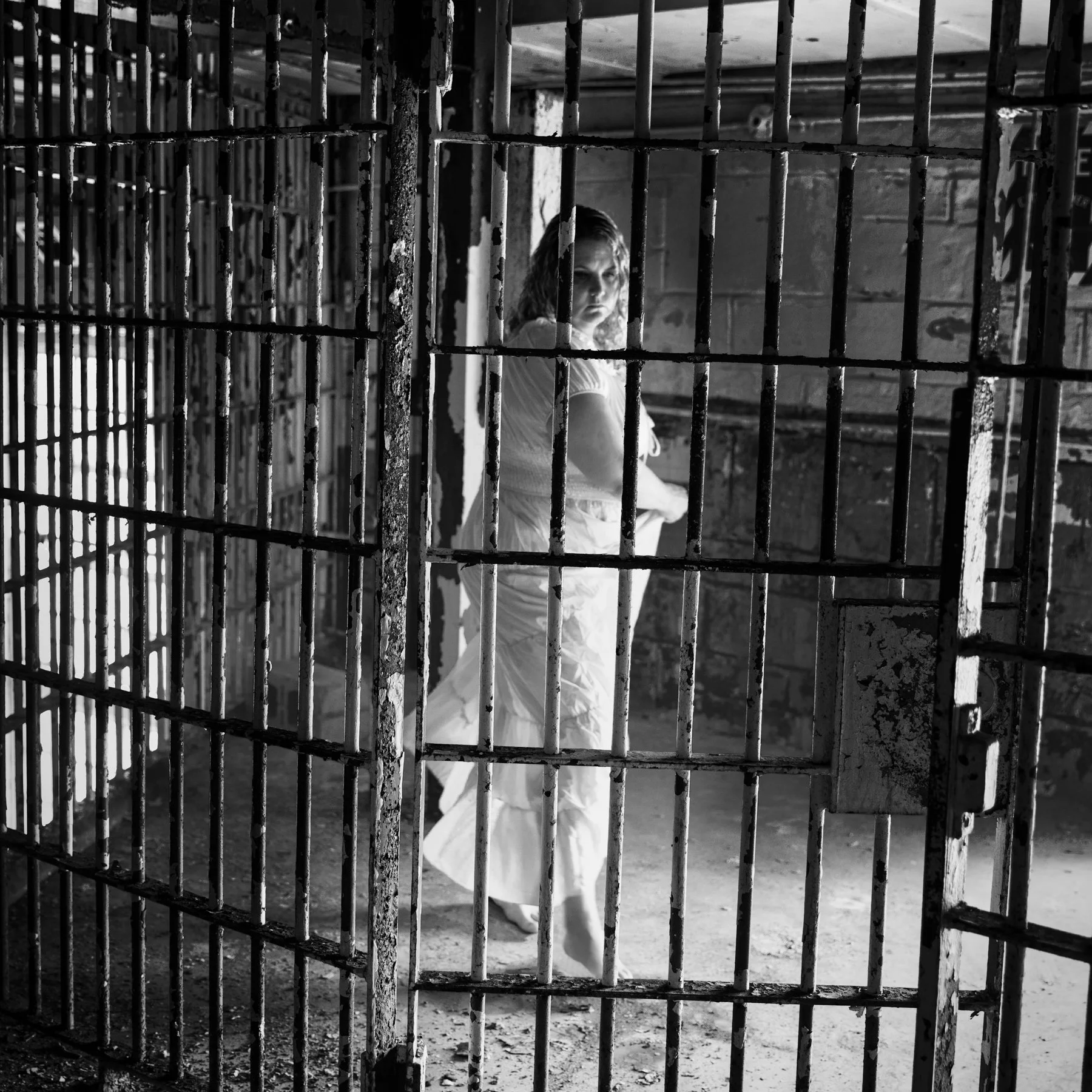 Black and white photo of woman in dress dancing in a jail cell