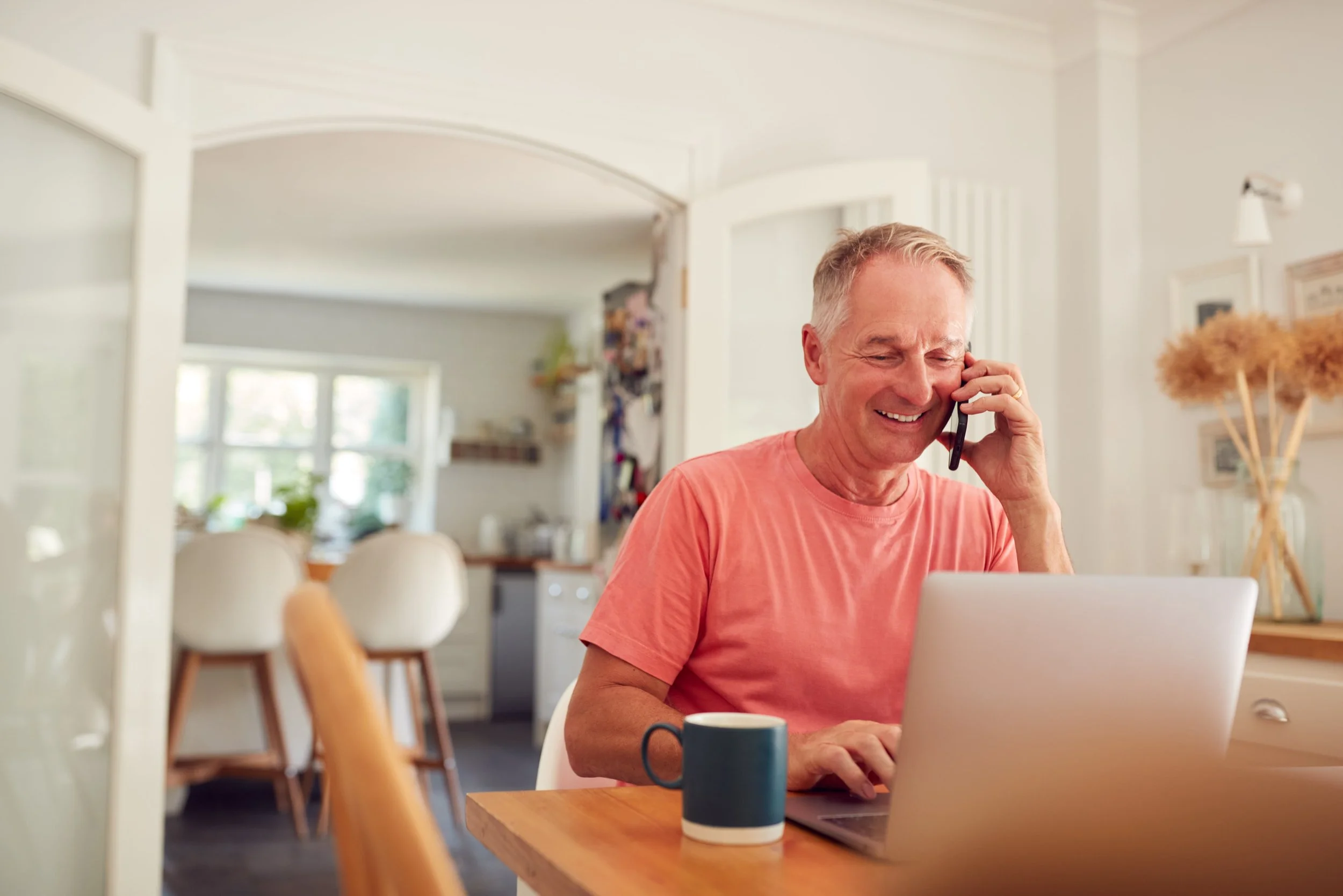 retired-man-on-phone-at-home-in-kitchen-using-lapt-KBPPCLR-min.jpg