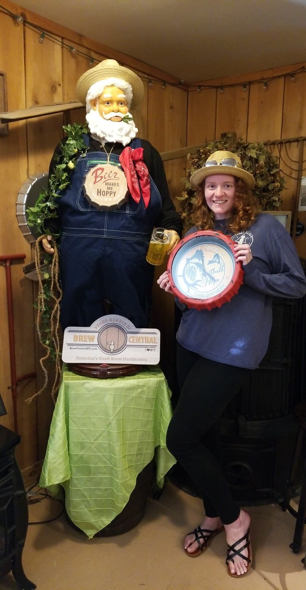 Animated Santa figure wearing overalls for harvest time with woman holding Foothill Hops branded clock.