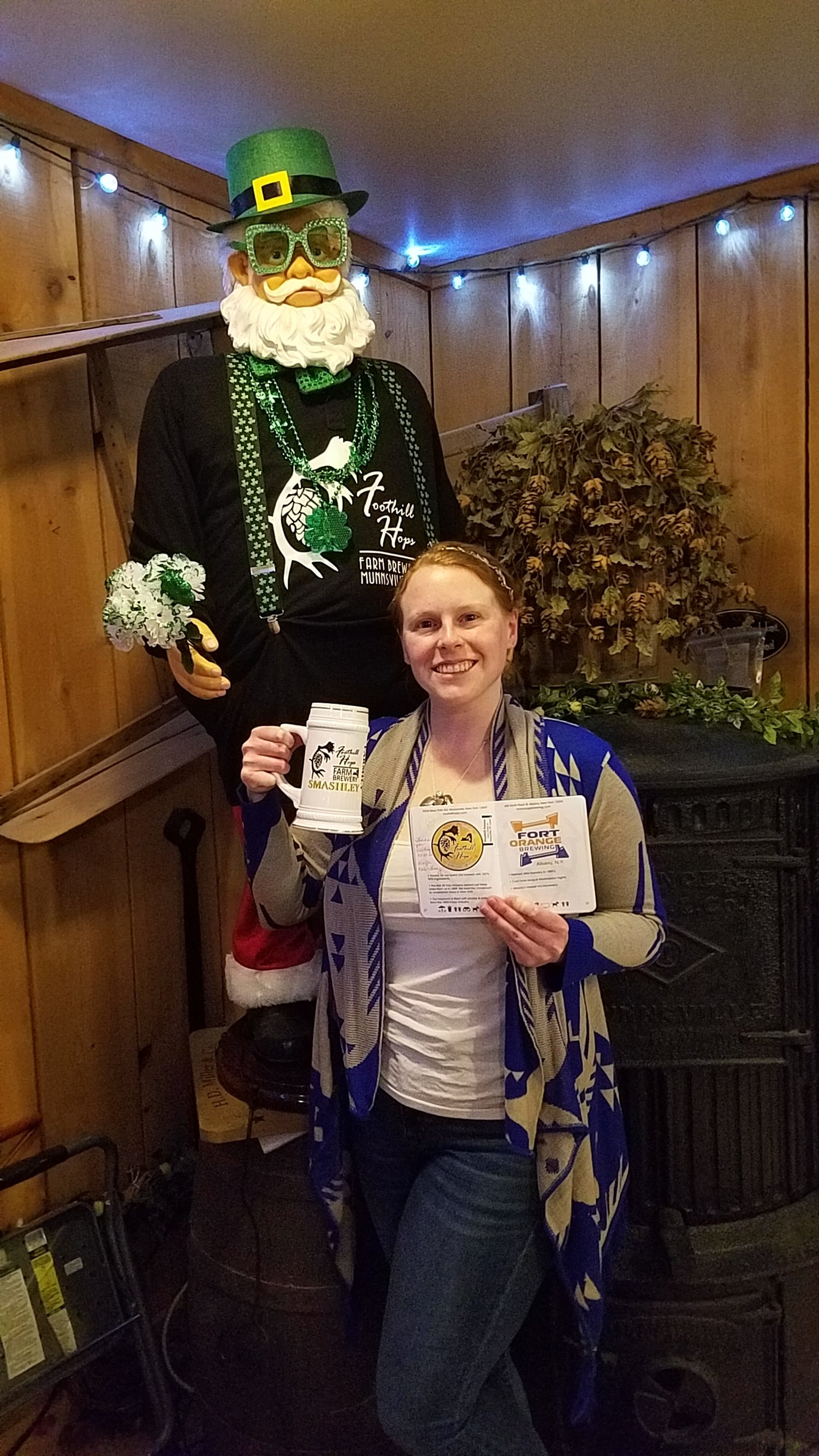Woman posing with mug in front of animated Santa dressed as leprechaun