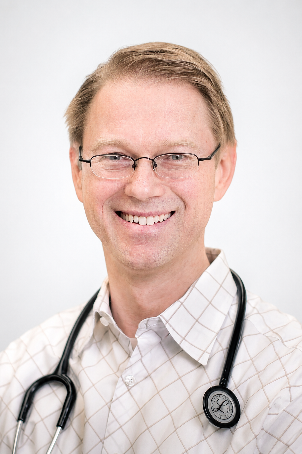 Dr Robert Ziegler, wearing a white checked shirt and a stethoscope around his neck, against a plain background.