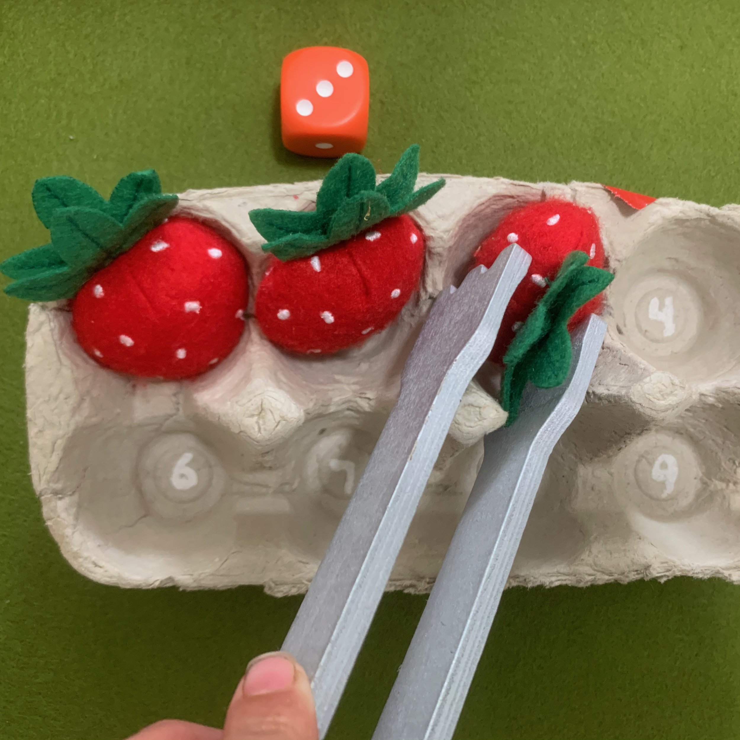  A counting game where two kids take turns rolling a dice and count in the language the number they roll while they move that many strawberries into the numbered egg carton. 