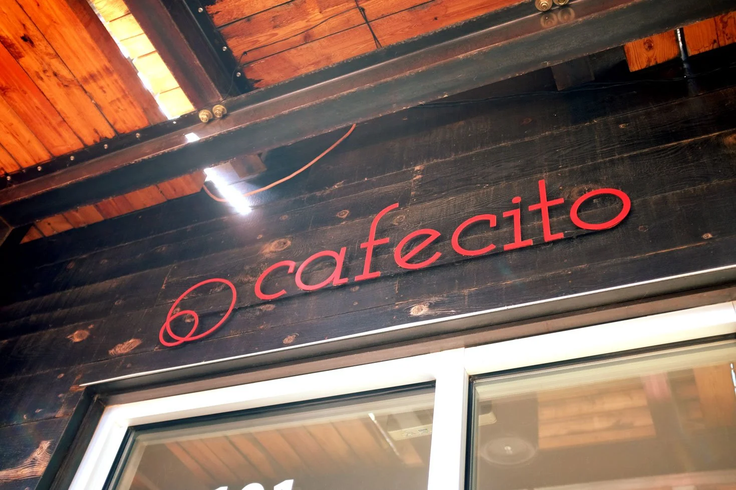 Red sign with the words 'O cafecito' mounted on dark stained wooden wall beneath a wooden ceiling.