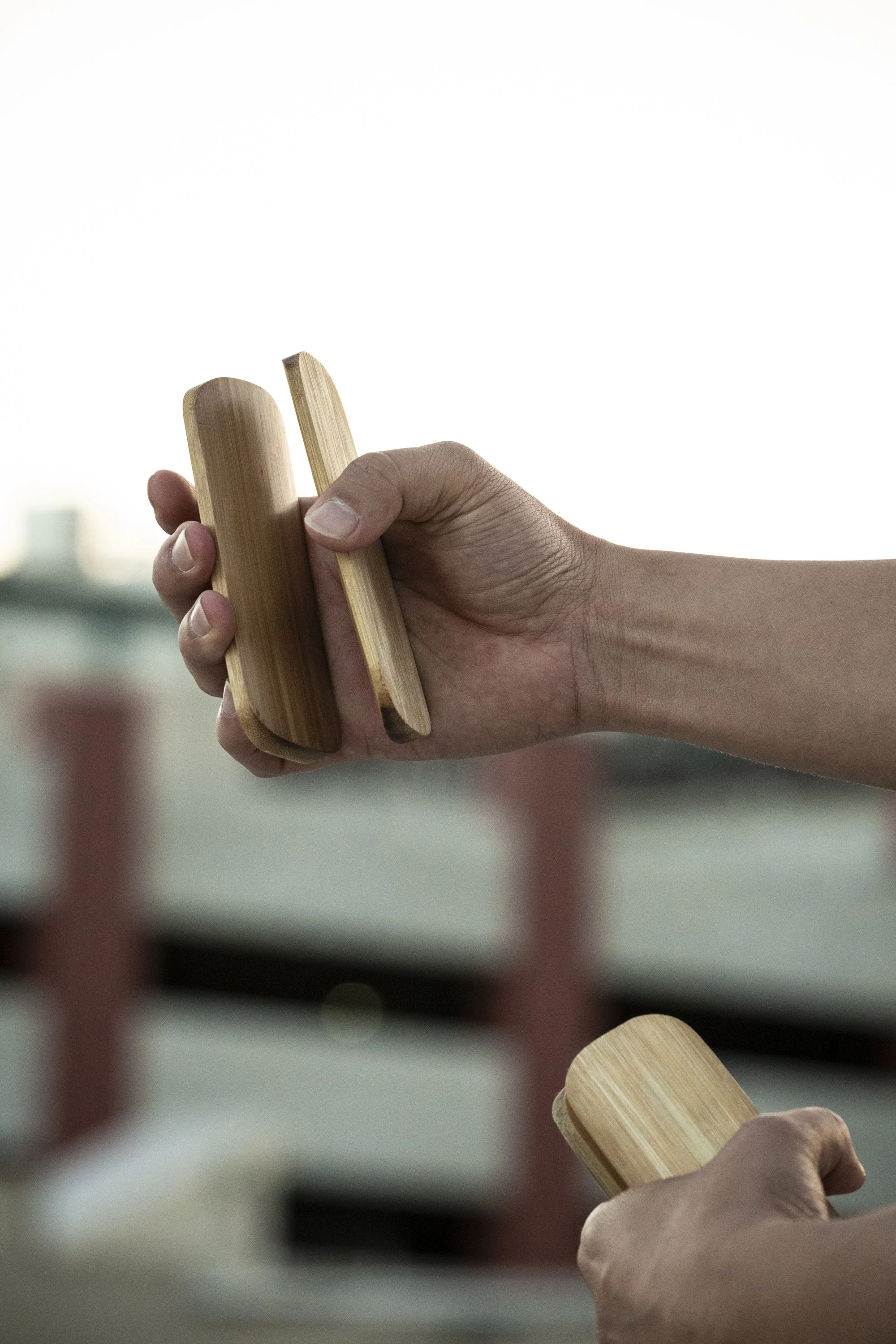 Close-up of a hand holding wooden pegs or tools, with a blurred background of red barriers and a white area.