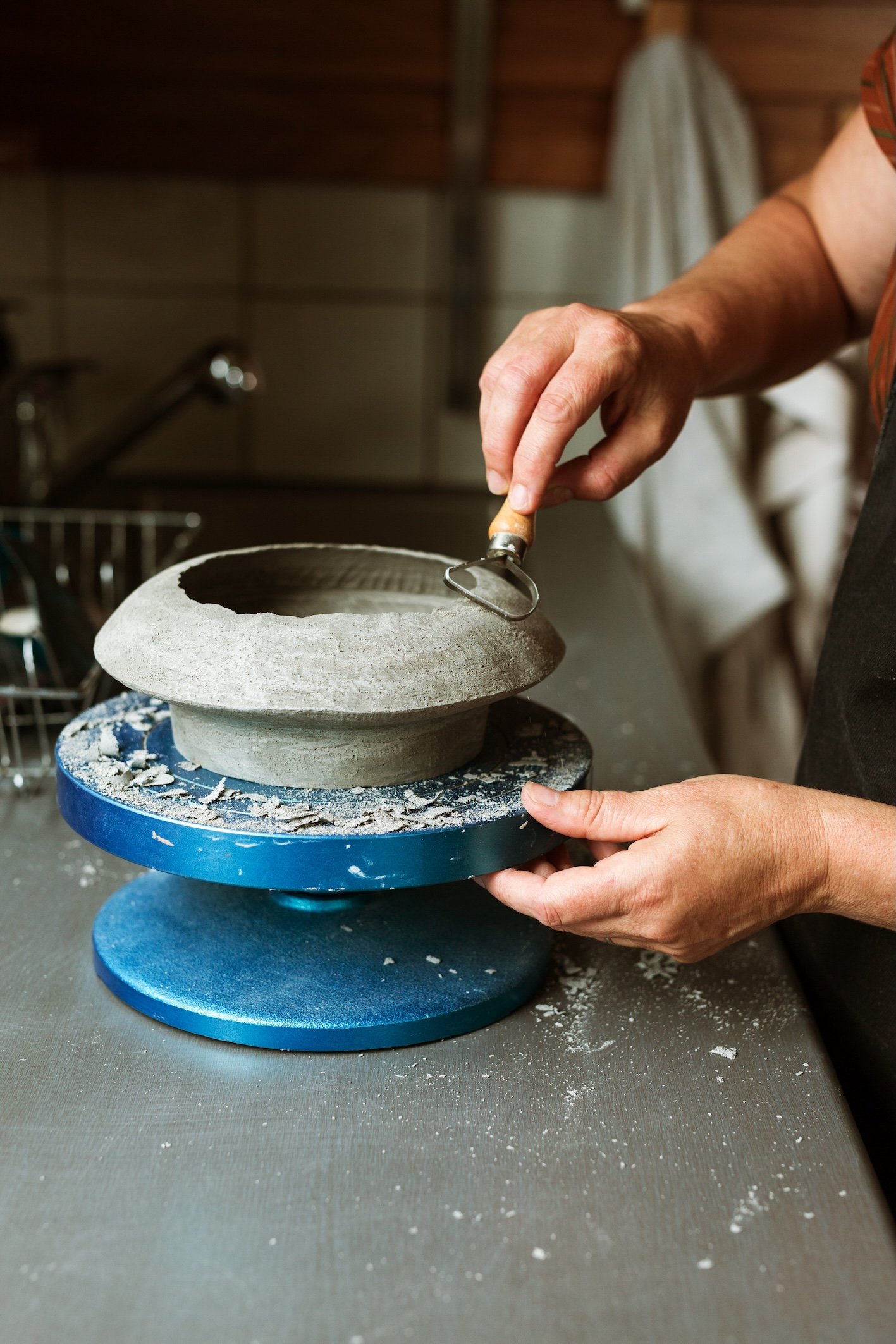 Lynda Wilson shaping a clay bowl on a pottery wheel in a ceramic studio.