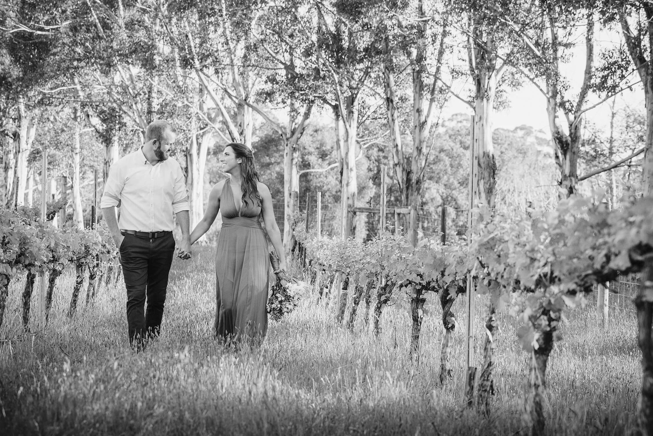 bride and groom walk through vineyard hand in hand with stunning forest backdrop.jpg