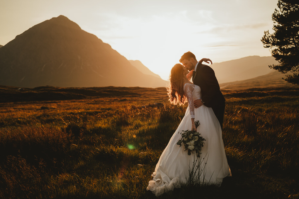 wedding photographer scotland prices shoot featuring a bride and groom in the country embracing at sunset with hills visible in the background