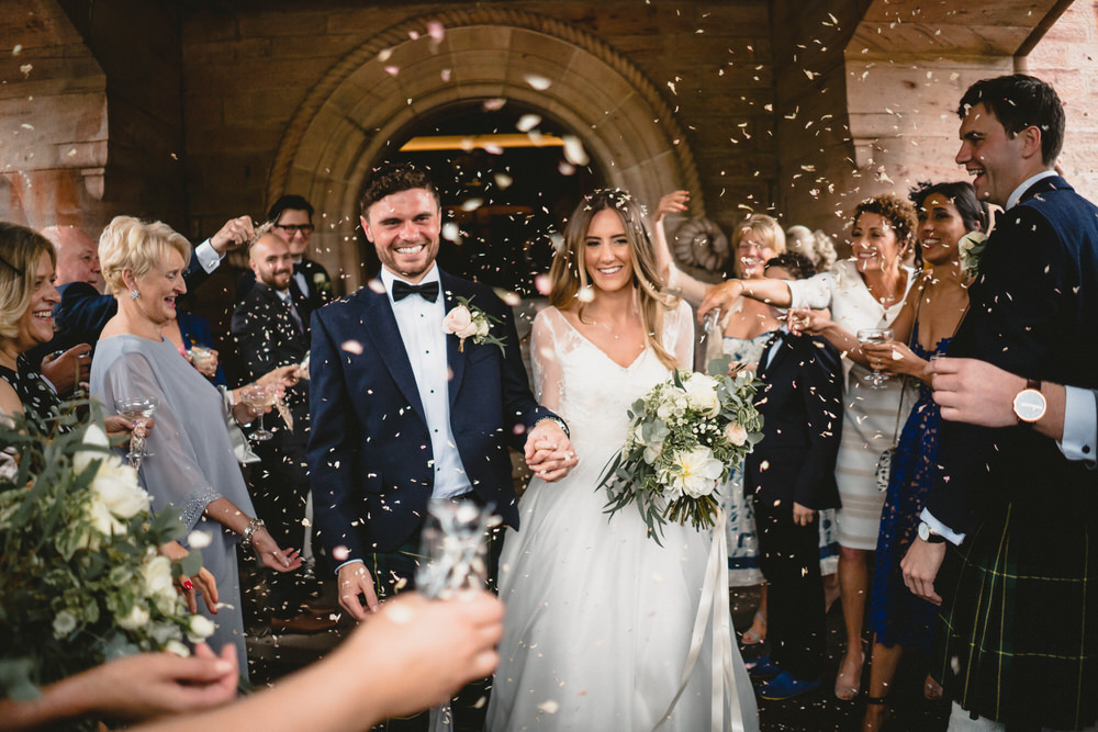 wedding photographer scotland prices captures bride and groom exit the ceremony venue hand in hand as guests throw confetti