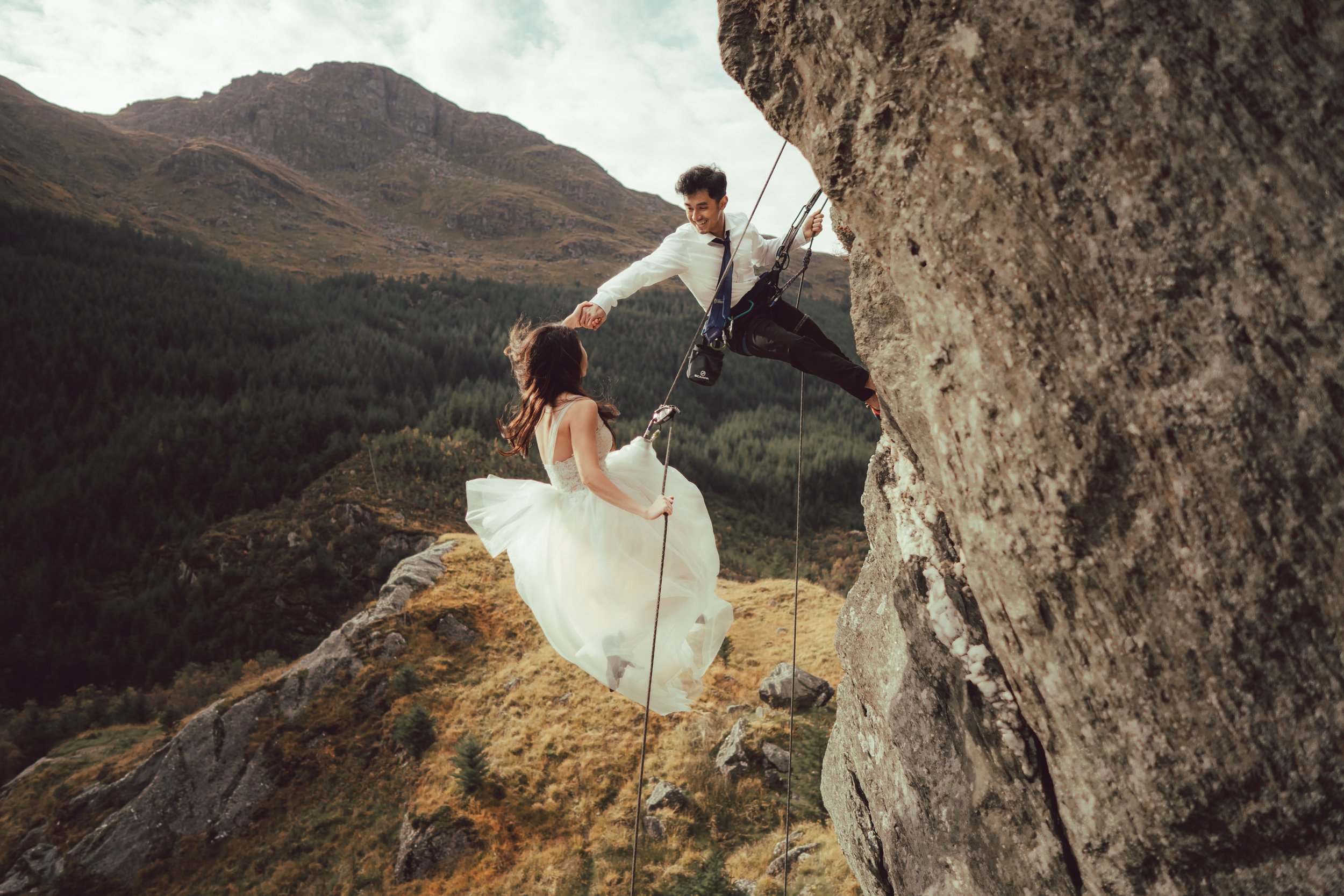 a bride in a white wedding gown and her groom abseil down a mountain captured by a glasgow wedding photographe