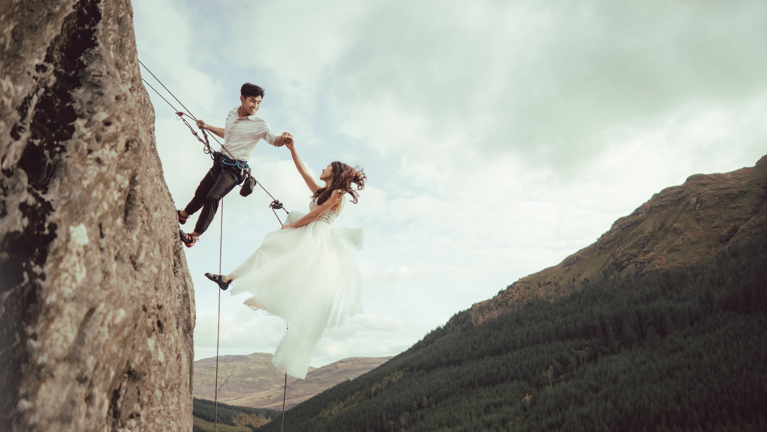 a bride in a white wedding gown and her groom abseil down a mountain captured by a glasgow wedding photographer