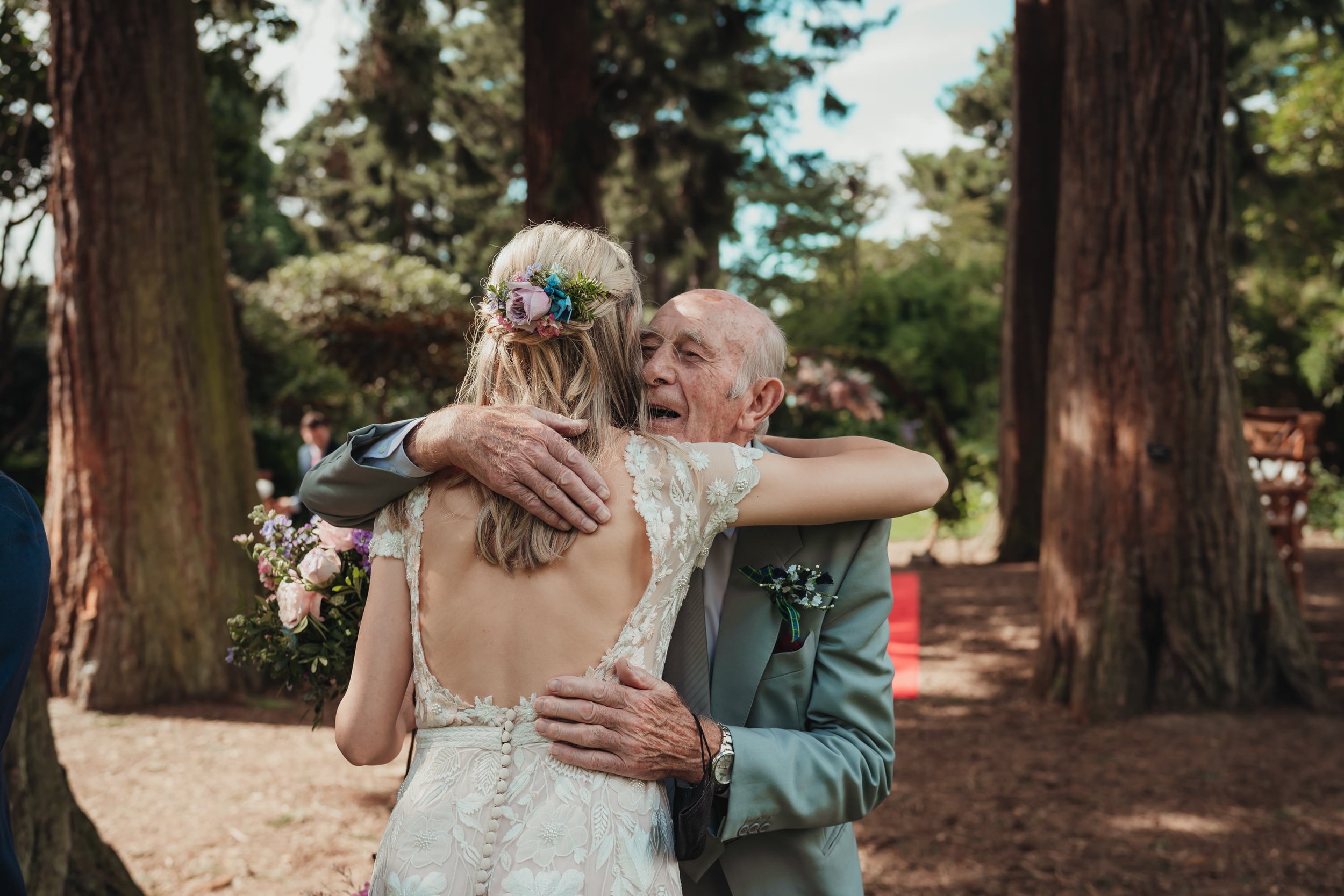 glasgow wedding photographer captures the bride hugging a guest in a wooded area with trees visible in the background