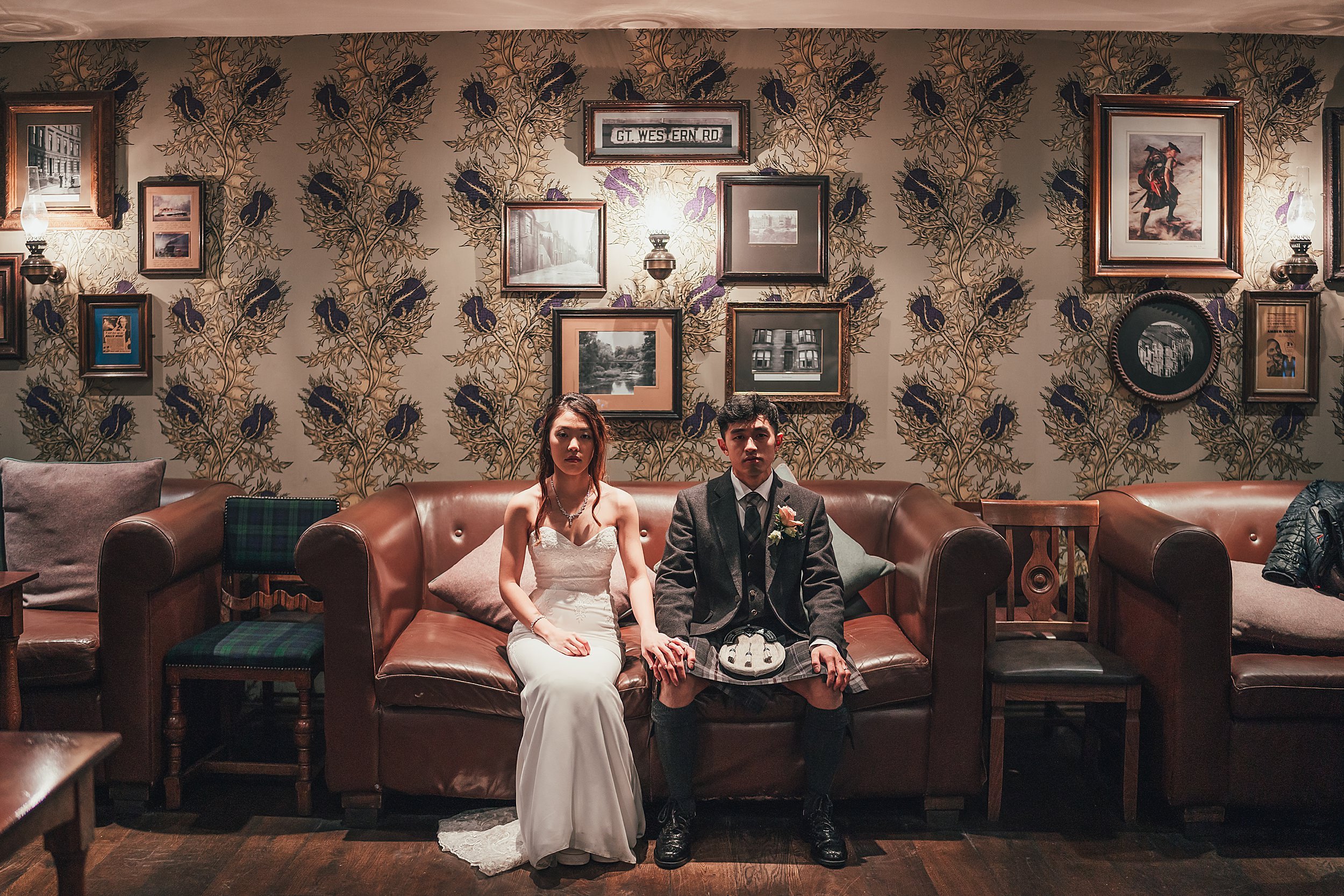 Chinese bride and groom sit on sofa on their wedding day at The Bothy Glasgow