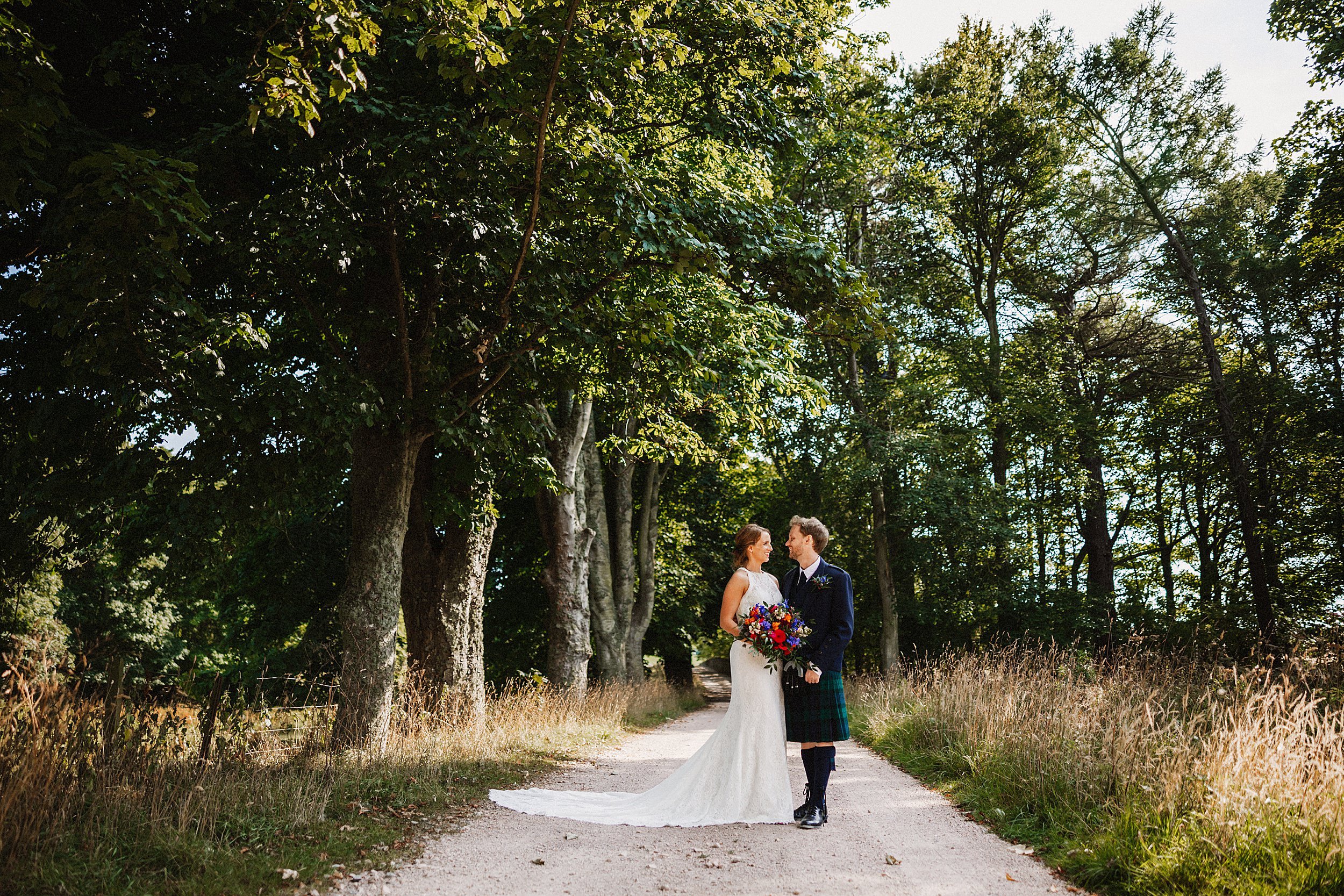Bride and groom walk through the grounds of a sunny Kinkell Byre on their wedding day in St Andrews