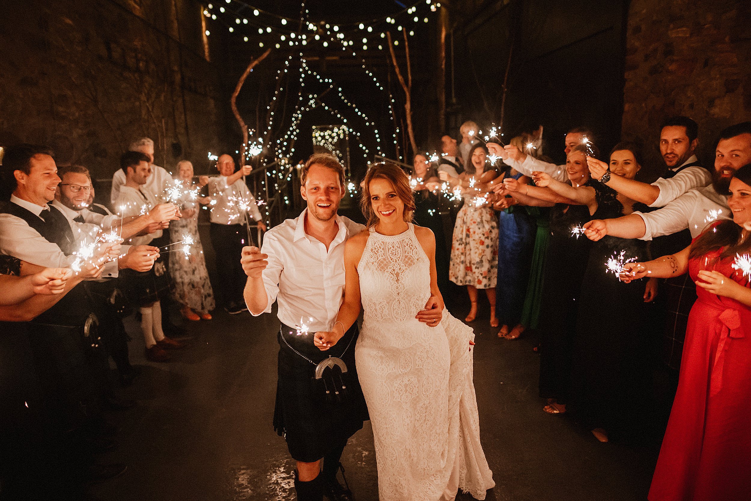 Bride and groom walk with sparklers on their wedding day with guests at Kinkell Byre St Andrews