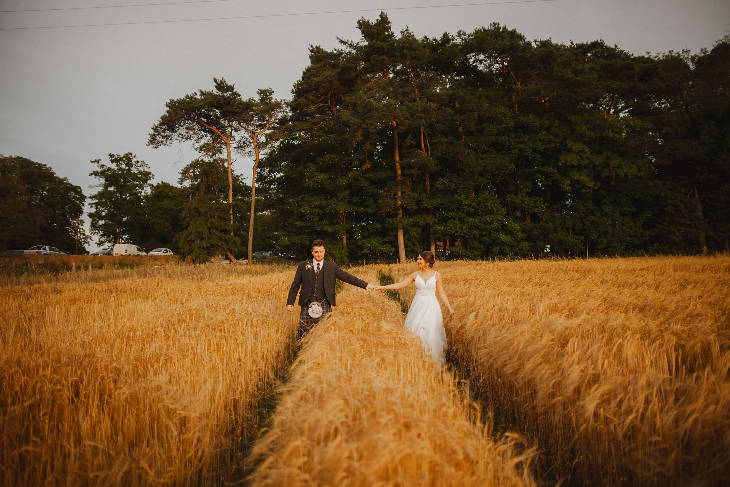 Bride and groom walk through a wheat field on their wedding day at Enterkine House Hotel