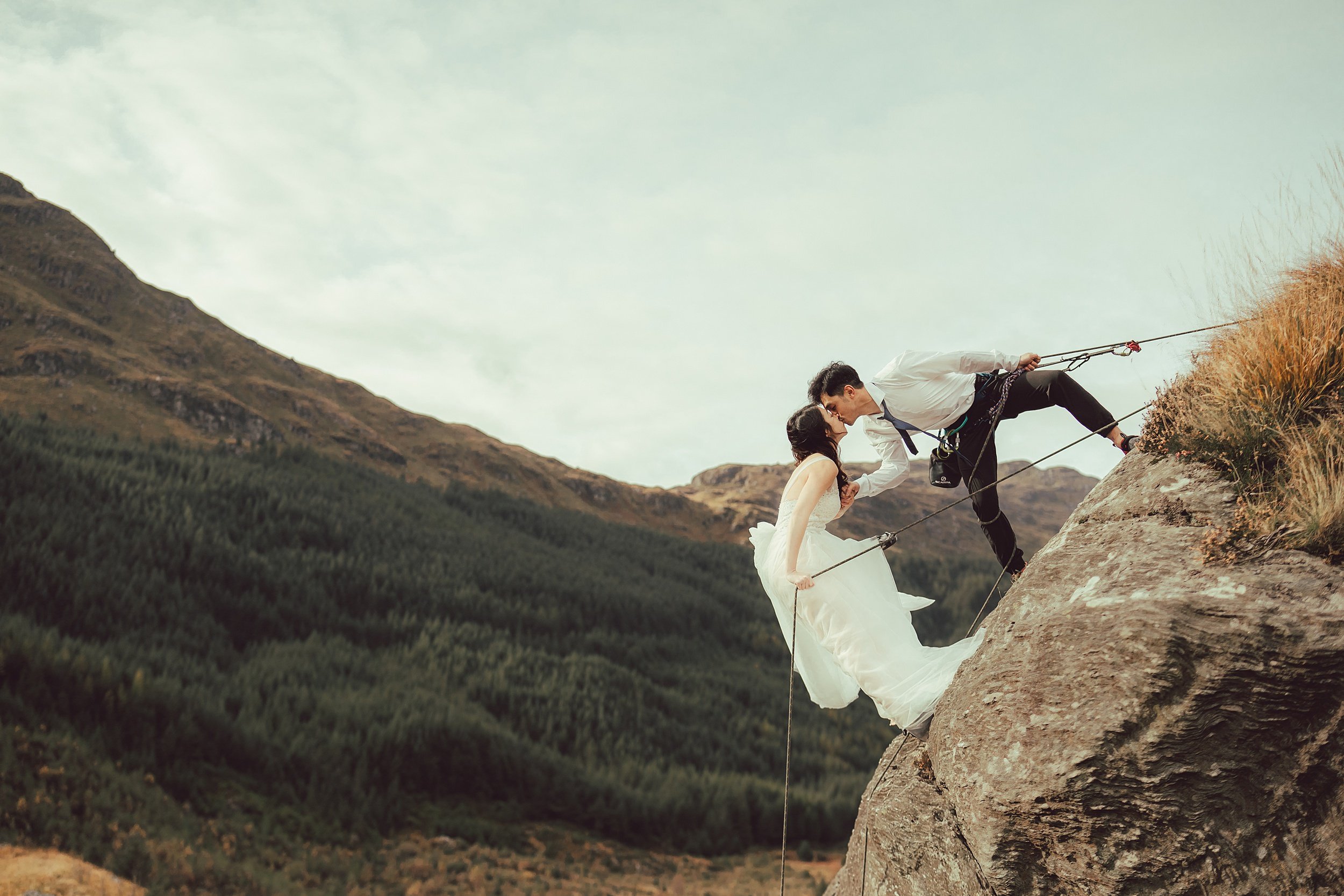 Bride and groom abseil off cliff face with kiss in Glencoe Skyfall valley