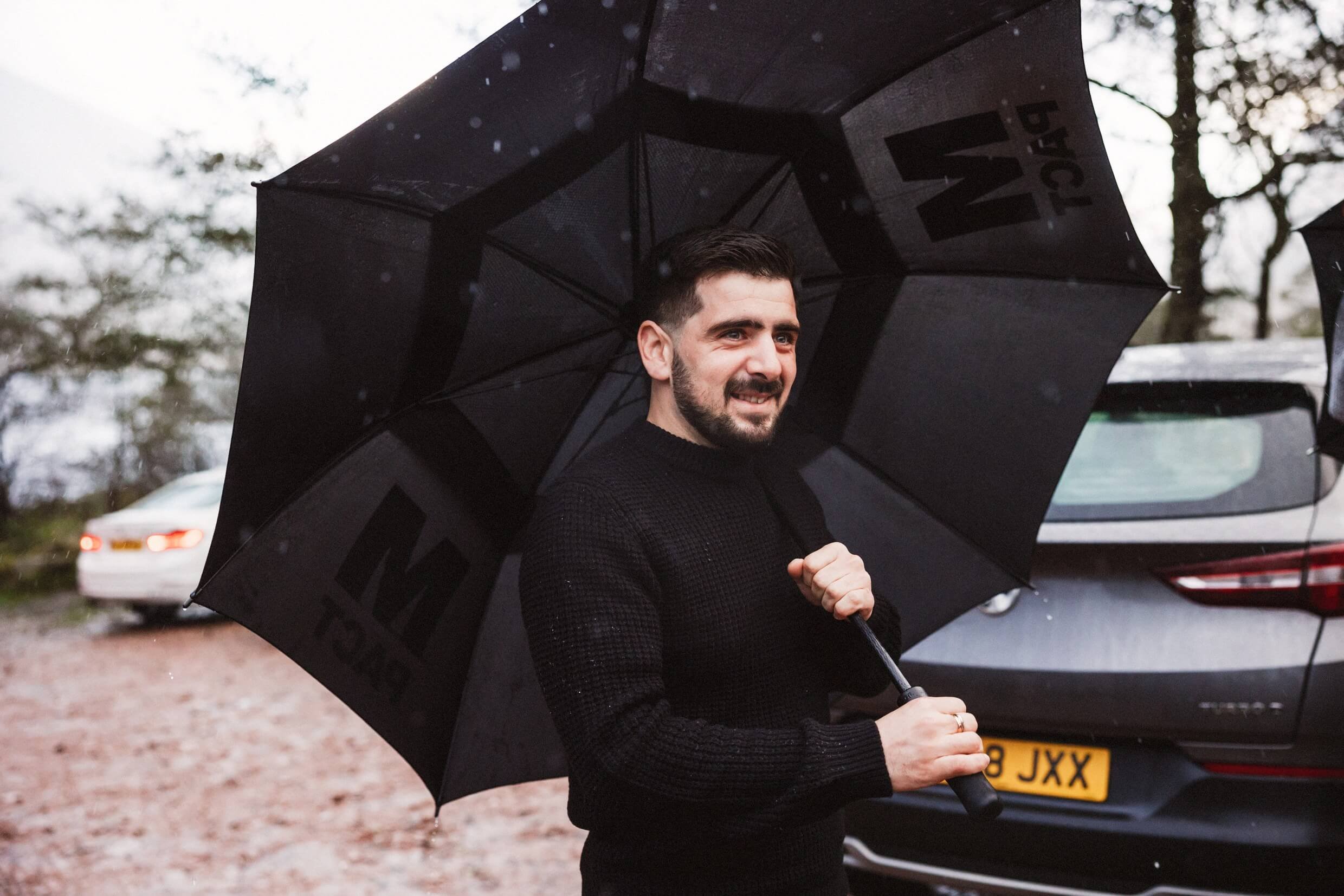 groom stands with umbrella during glencoe elopement