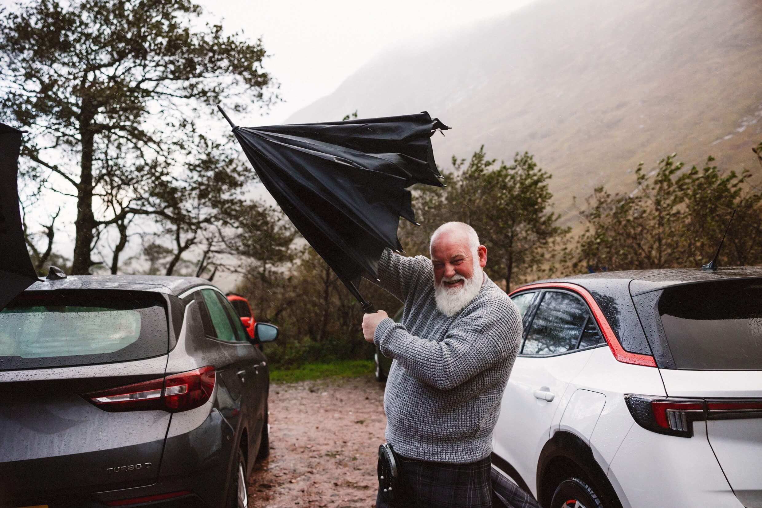 father of the bride struggles with umbrella in wet weather during glencoe elopement