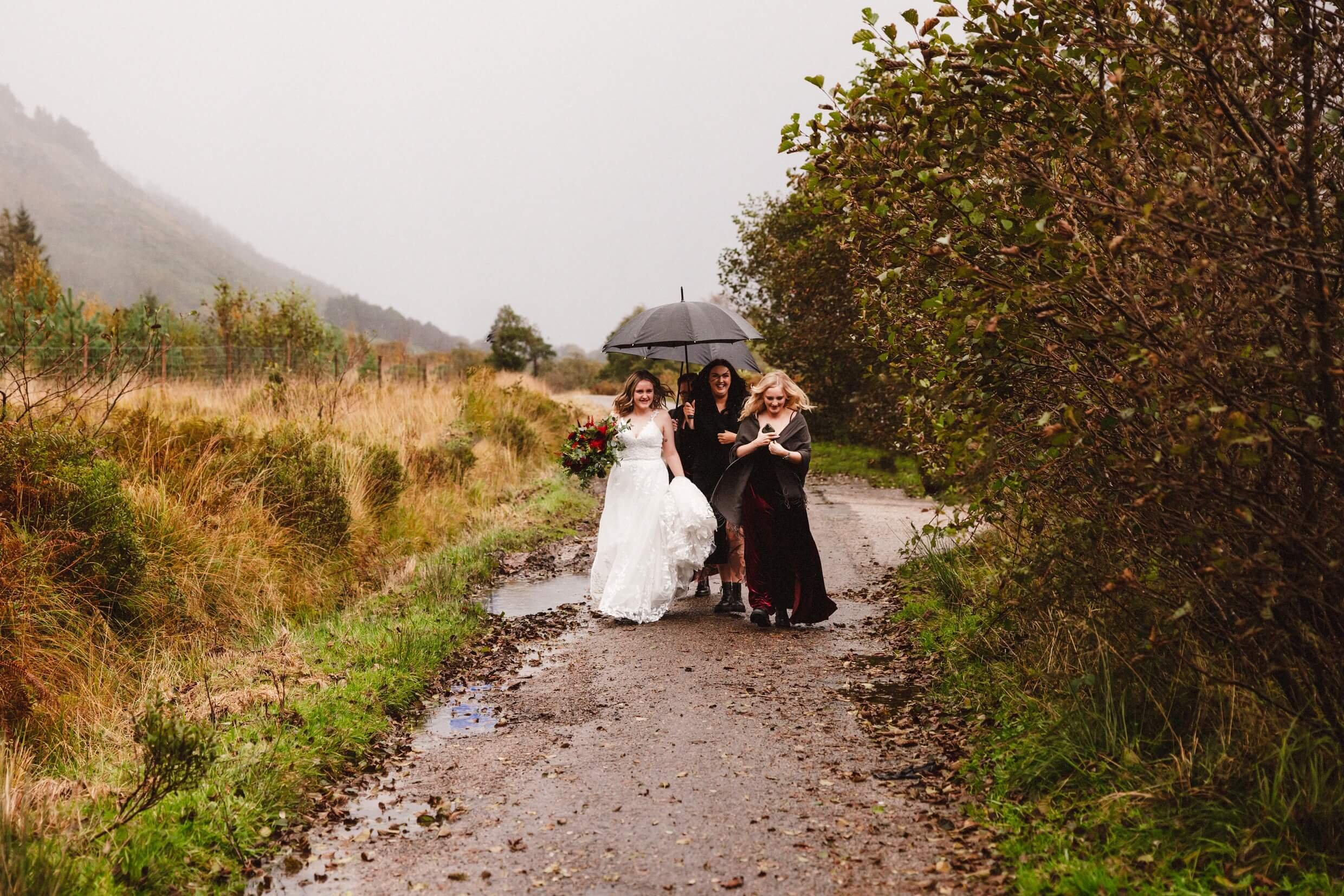 bride walks down underneath an umbrella for a micro wedding glencoe elopement at loch etive in scotland